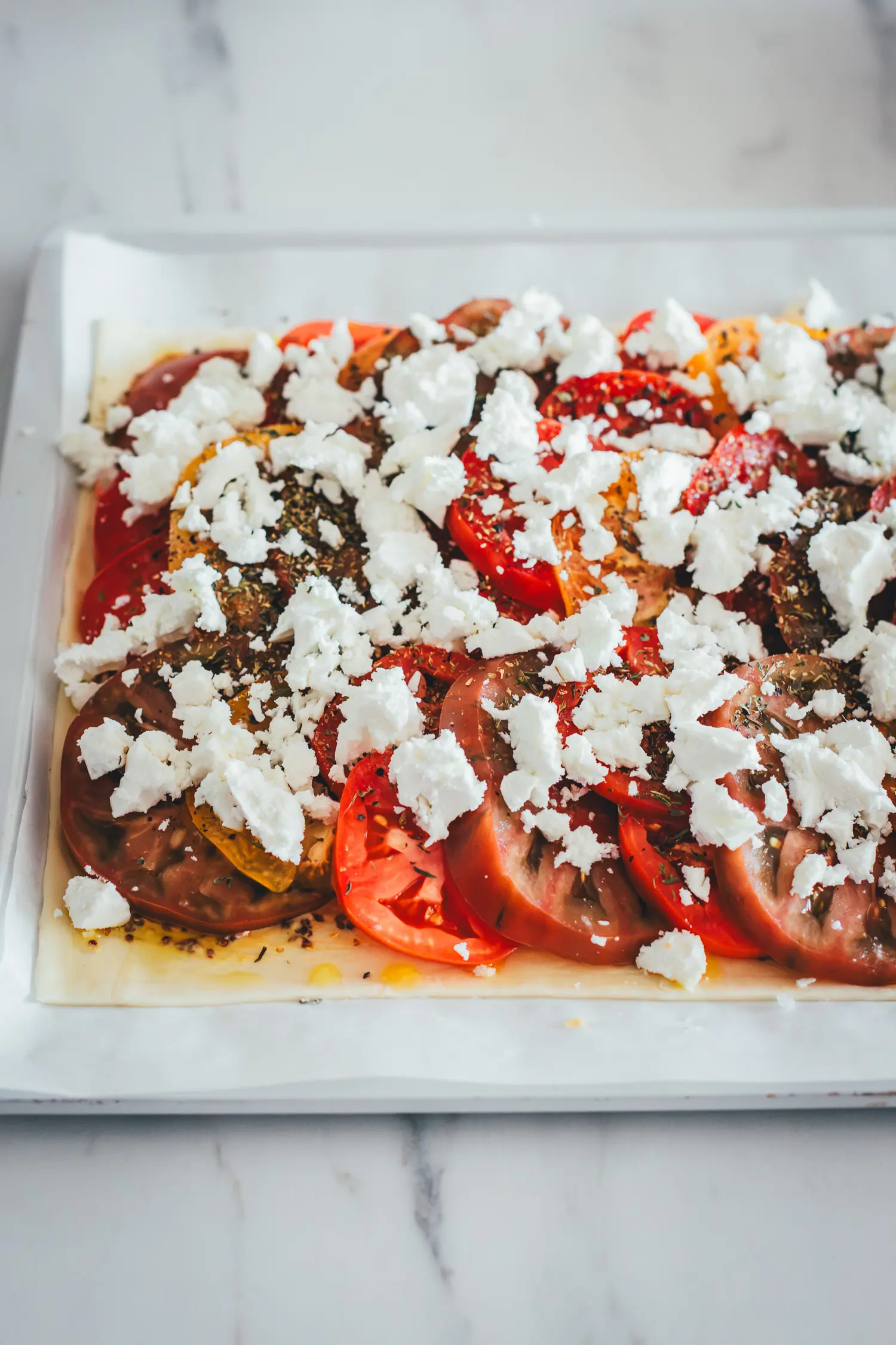 Bunte reife Tomaten in Scheiben auf Blätterteig mit Dijon- und Ancienne-Senf, getoppt mit Feta. Bereit zum Backen.