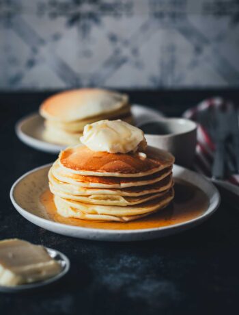 Pancakes – mein absolutes Lieblingsrezept seit über 15 Jahren. Einfach ein Stapel Pancakes mit Butter und Ahornsirup serviert auf einem kleinen Teller | moeyskitchen.com