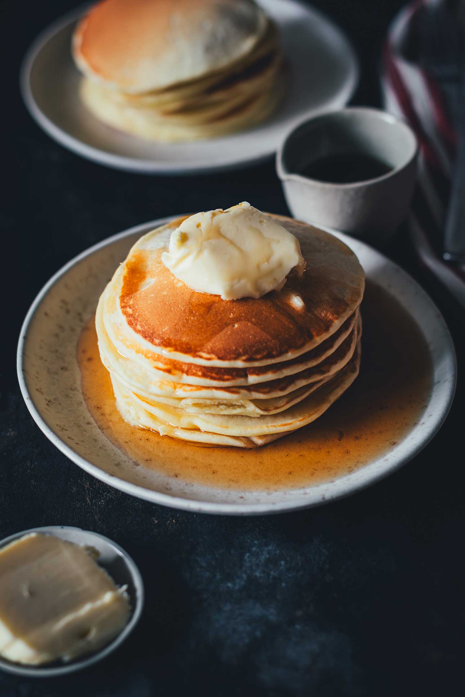 Seitliche Nahaufnahme eines Pancake-Stapel mit Butter und Ahornsirup auf einem Teller | moeyskitchen.com