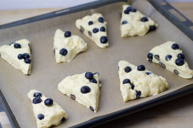 Rezept für Blueberry-Cream-Scones mit Clotted Cream und Marmelade zum Sonntagsfrühstück Die Teigstücke für die Scones mit Blaubeeren und Sahne werden auf ein Backblech gesetzt