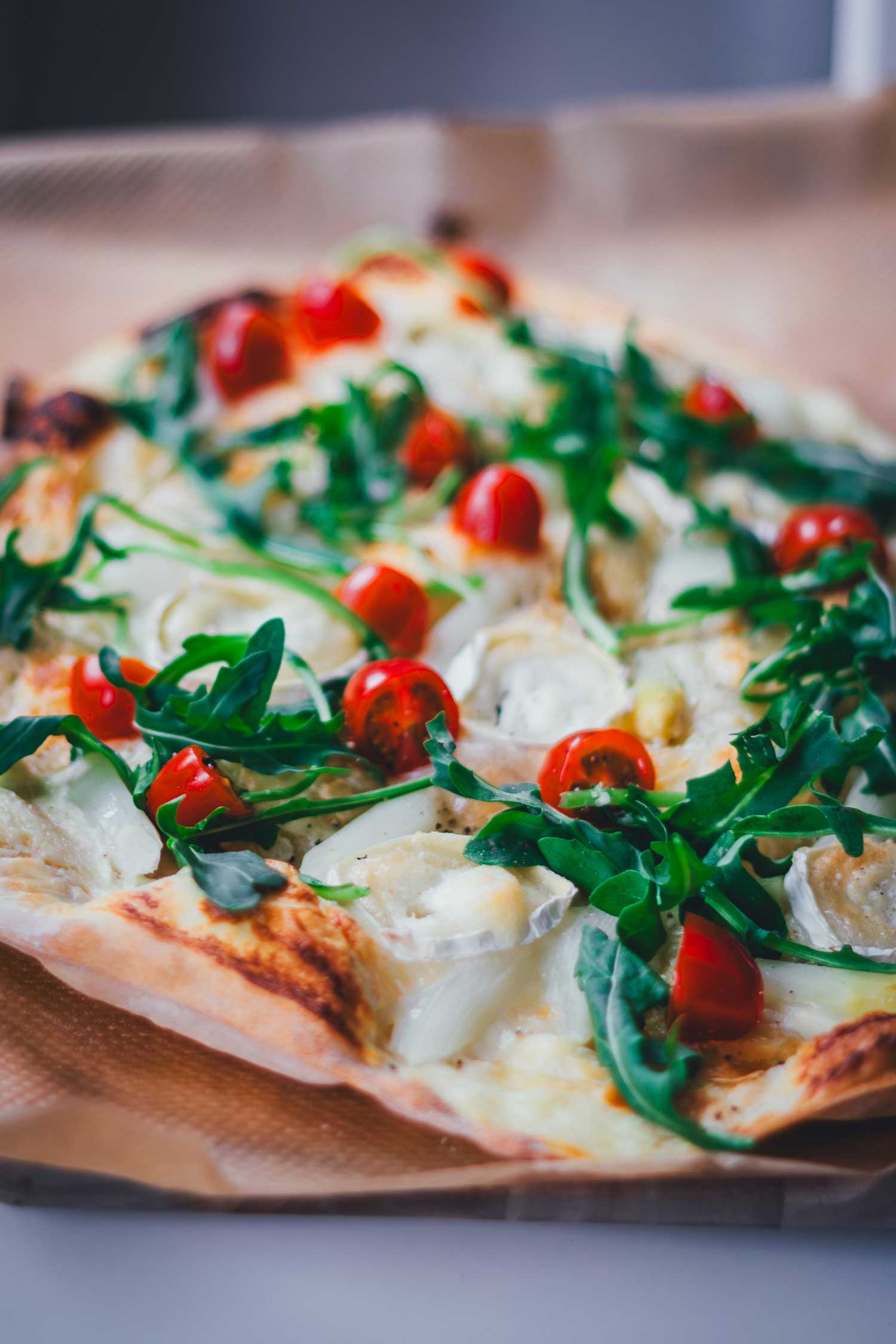 Flache Nahaufnahme von einem frisch gebackenen, knusprigen Flammkuchen mit weißem Spargel, Tomaten, Rucola und Ziegenkäse.