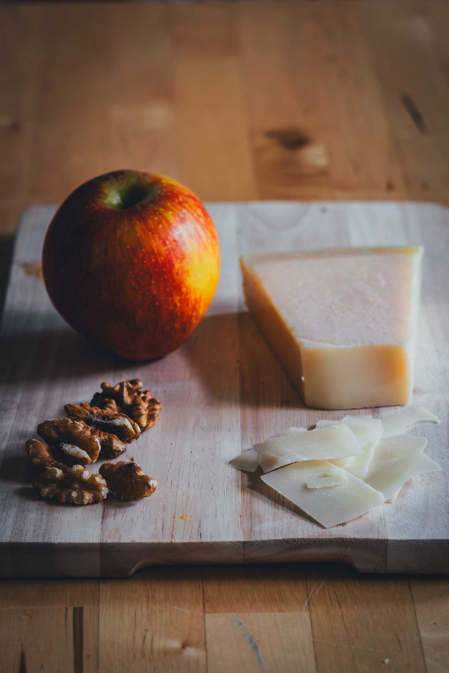 Zutaten für Rosenkohlsalat: Apfel, Walnüsse und Pecorino auf Holzbrett