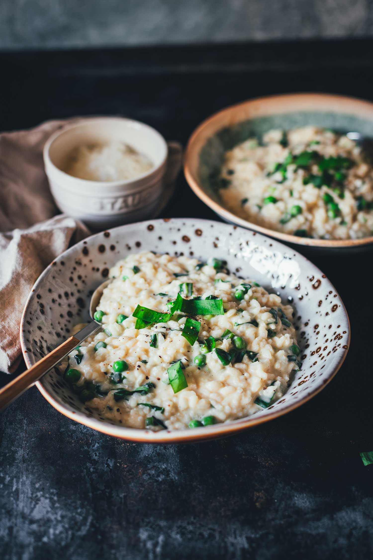 Seitlicher Blick auf einen Teller mit Bärlauch-Risotto. Das cremige Risotto wird mit frischem Bärlauch getoppt und mit geriebenem Käse serviert.