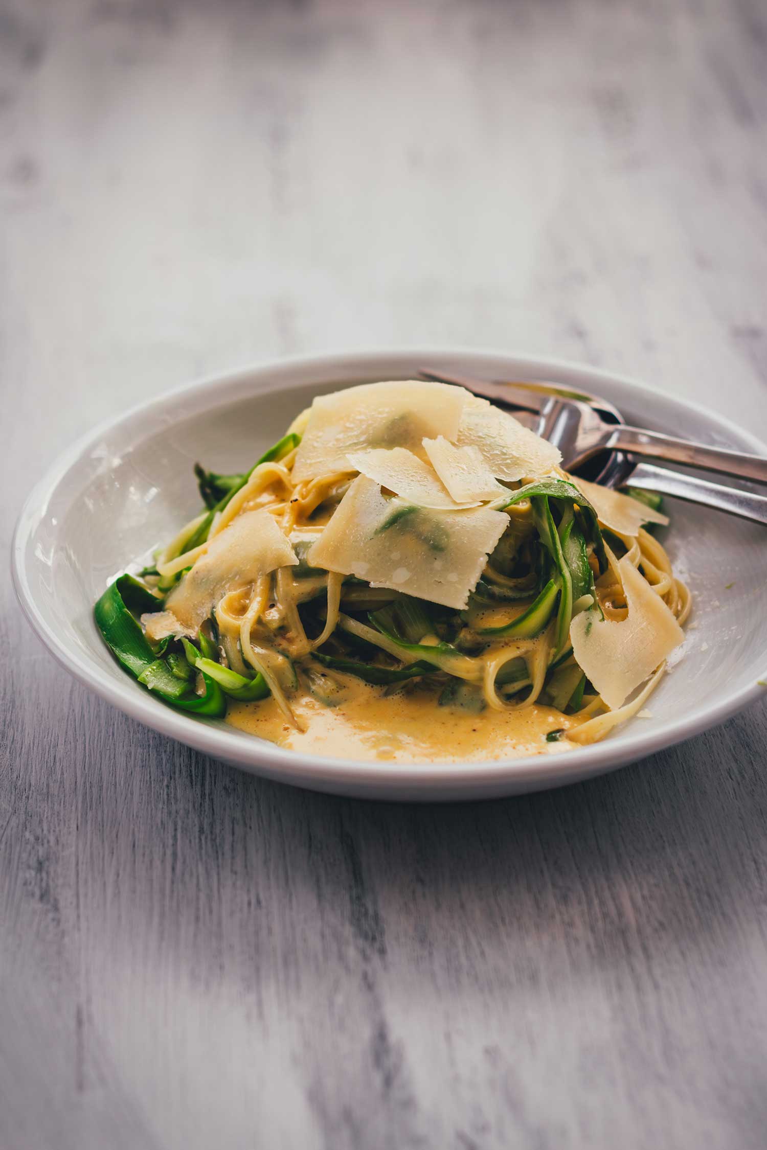 Linguine mit grünem Spargel und Parmesansauce seitlich auf einem Teller fotografiert.