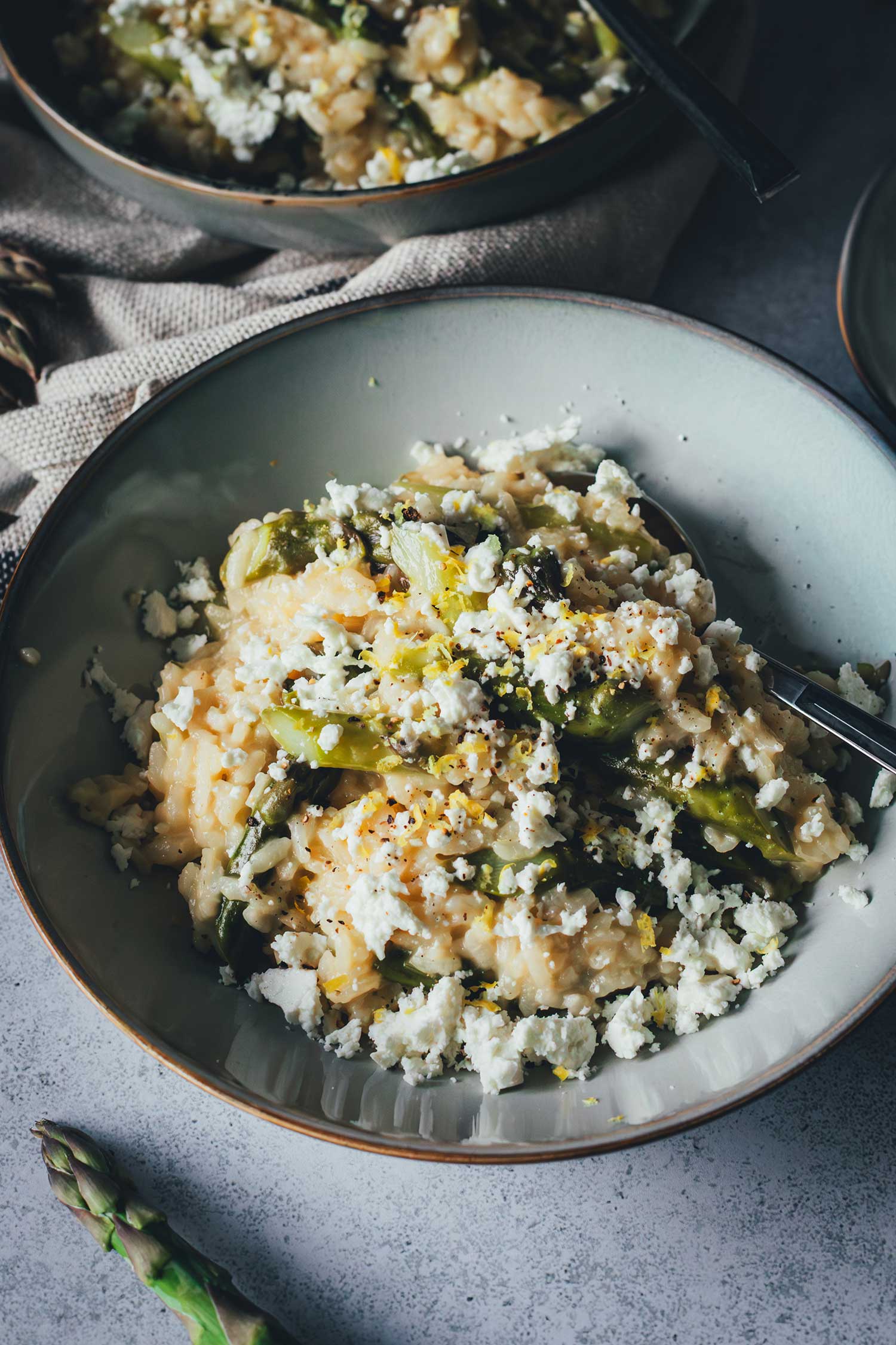 Nahaufnahme einer Schale Ofenrisotto mit grünem Spargel, zerbröckeltem Feta und frisch abgeriebener Zitronenschale