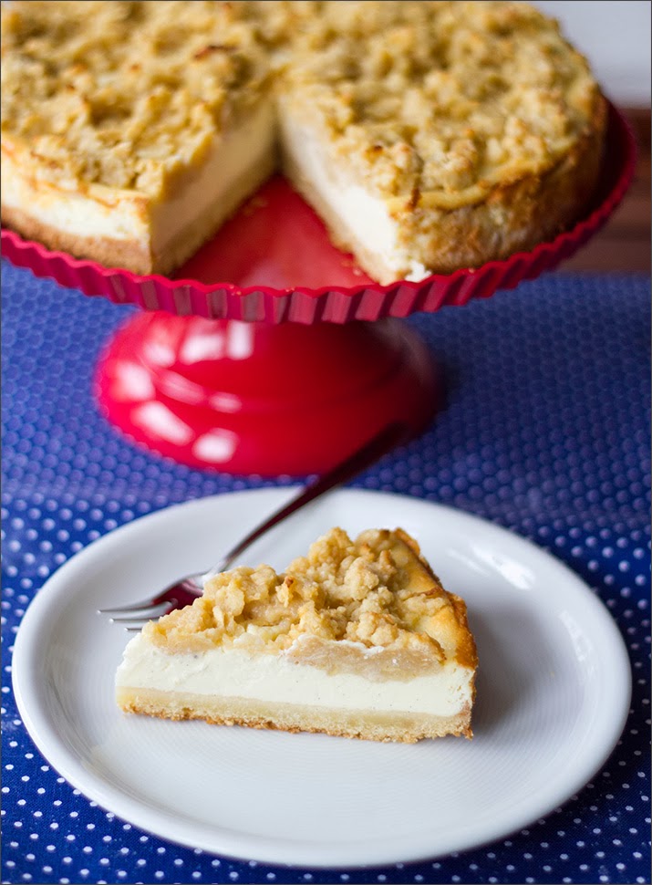 Vanille-Cheesecake mit Apfel-Streuseln Angeschnittener Vanille-Käsekuchen mit Apfel-Streuseln auf Kuchenplatte, Kuchenstück auf Teller