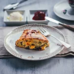 Himbeer Scones mit Pistazien und weißer Schokolade, frisch gebacken und mit Zucker bestreut, serviert mit Clotted Cream und Konfitüre