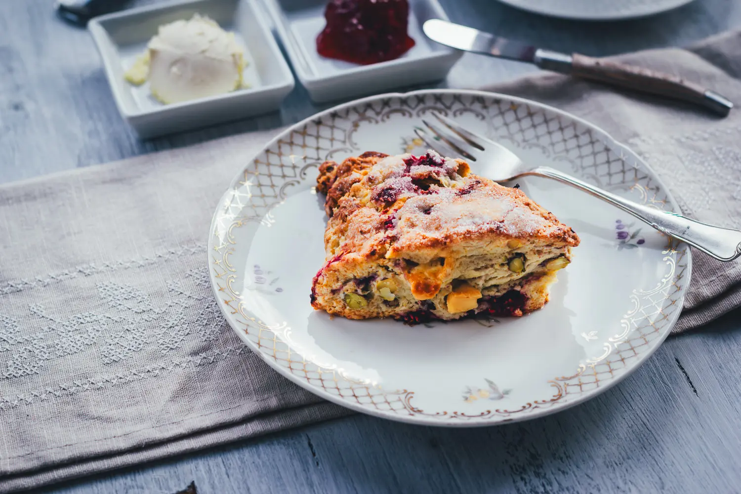 Himbeer Scone mit karamellisierter weißer Schokolade und Zuckerkruste auf einem Goldrand-Teller mit Leinenserviette