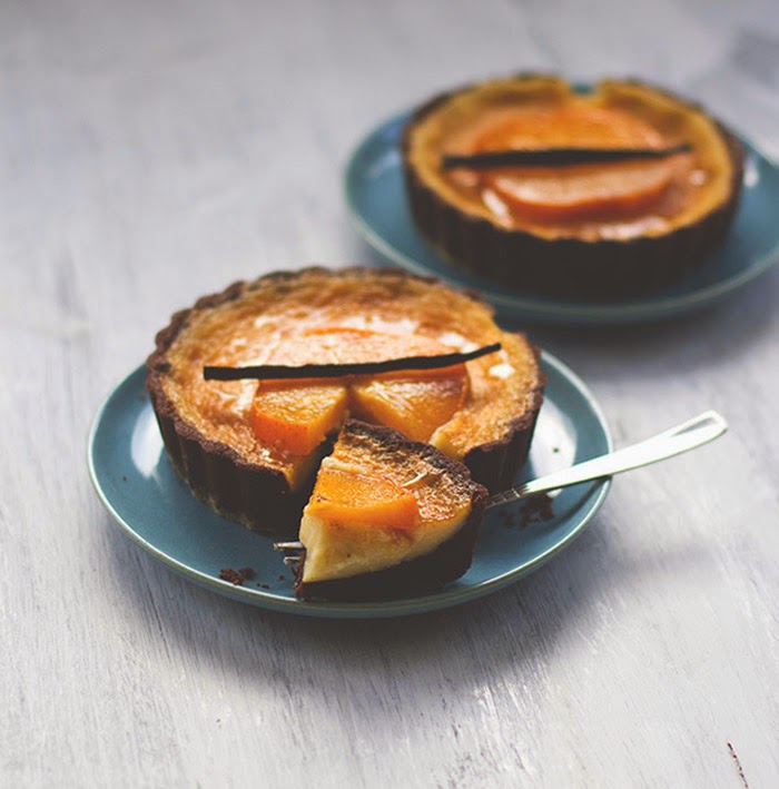 Angeschnittene Kakao-Tartelettes mit einer Füllung aus weißer Schokolade und Sahne, belegt mit Kakis in Vanillesirup