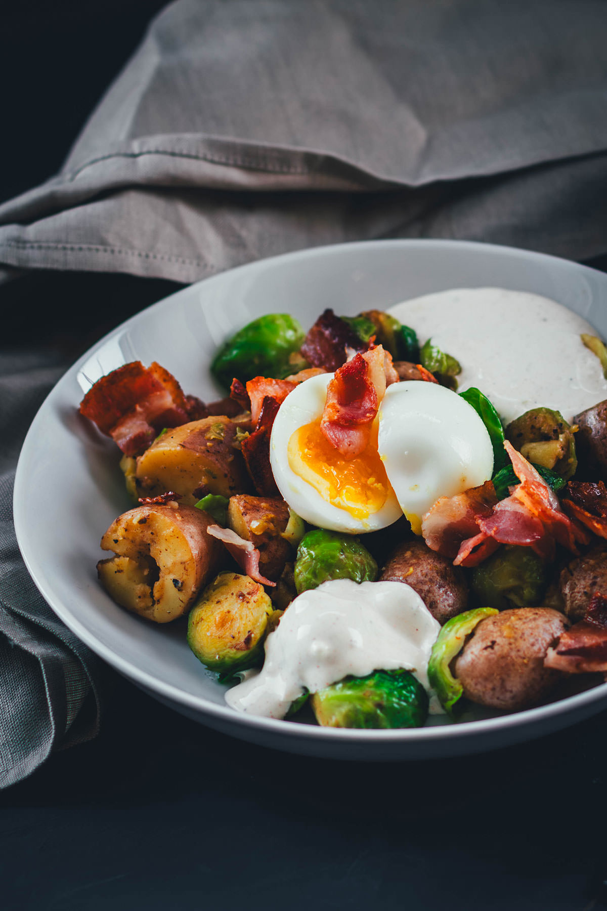 Hier teile ich mein Rezept für eine deftige Rosenkohl-Kartoffel-Pfanne. Serviert mit wachsweichem Ei, knusprigem Bacon und würzigem Knoblauch-Schmand. Perfekt für die schnelle Feierabendküche in Herbst und Winter! | moeyskitchen.com
