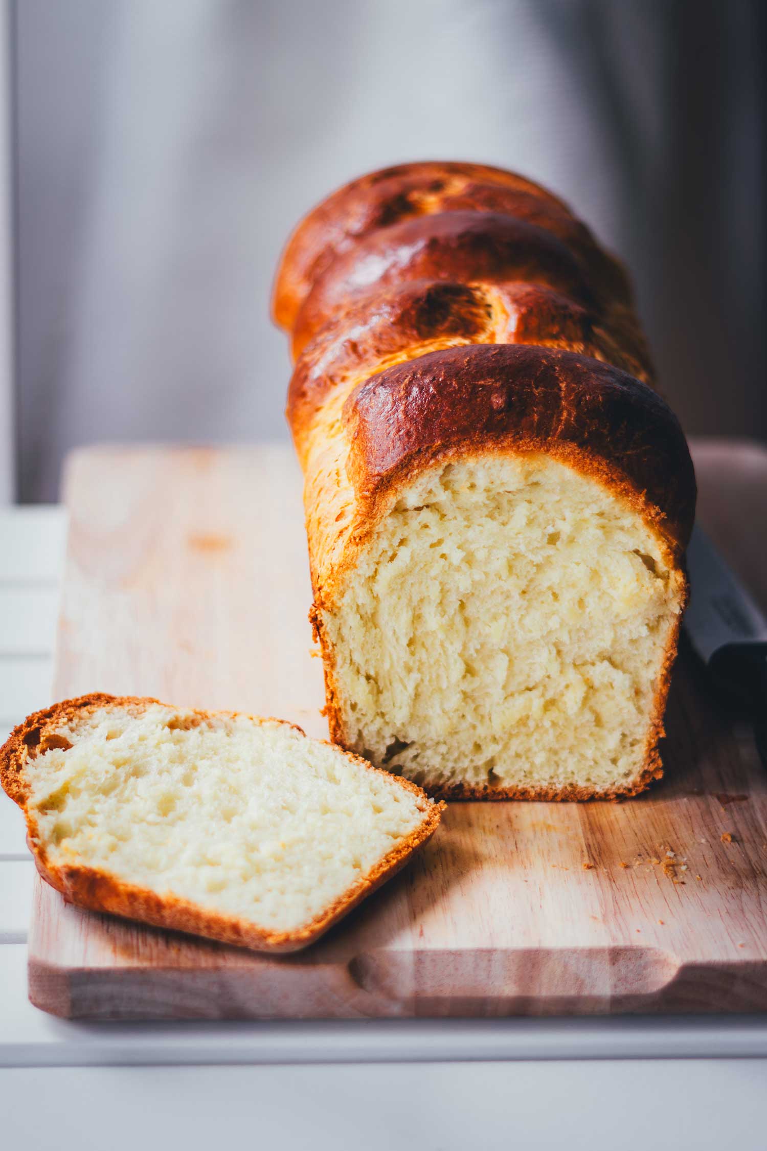 Frisch angeschnittene Brioche auf einem Holzbrett. Man sieht ein goldgelbes, weiches Brot im Anschnitt.
