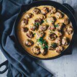 Köttbullar, schwedische Hackbällchen wie von IKEA werden in leckerer cremiger Sauce in einer gusseisernen Pfanne serviert. Die saftigen Hackbällchen sind mit Petersilie bestreut. Neben der Pfanne liegt ein Küchentuch. | moeyskitchen.com