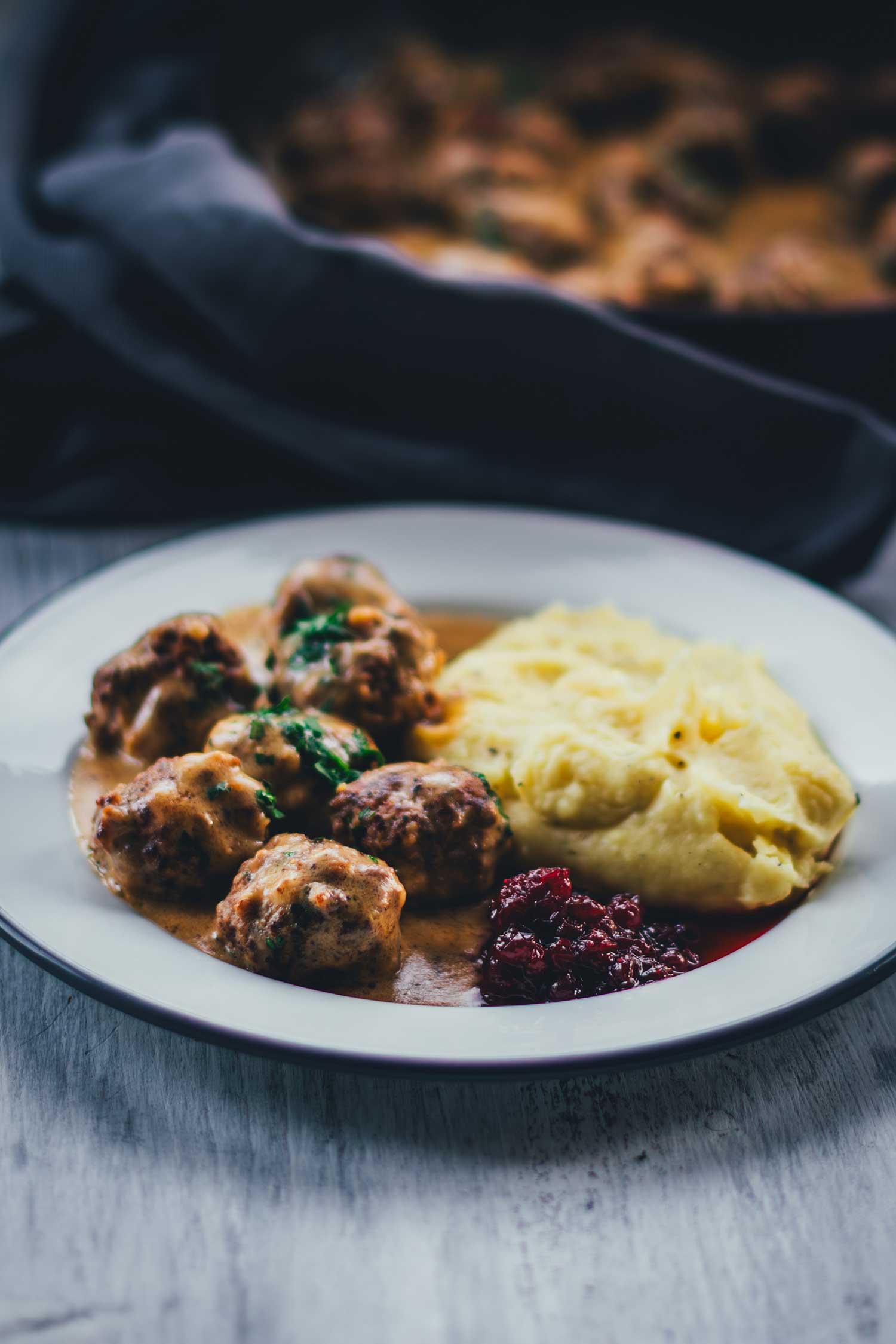 Nahaufnahme eines Tellers mit schwedischen Hackbällchen in sahniger Sauce, serviert mit Kartoffelbrei und Wildpreiselbeeren | moeyskitchen.com