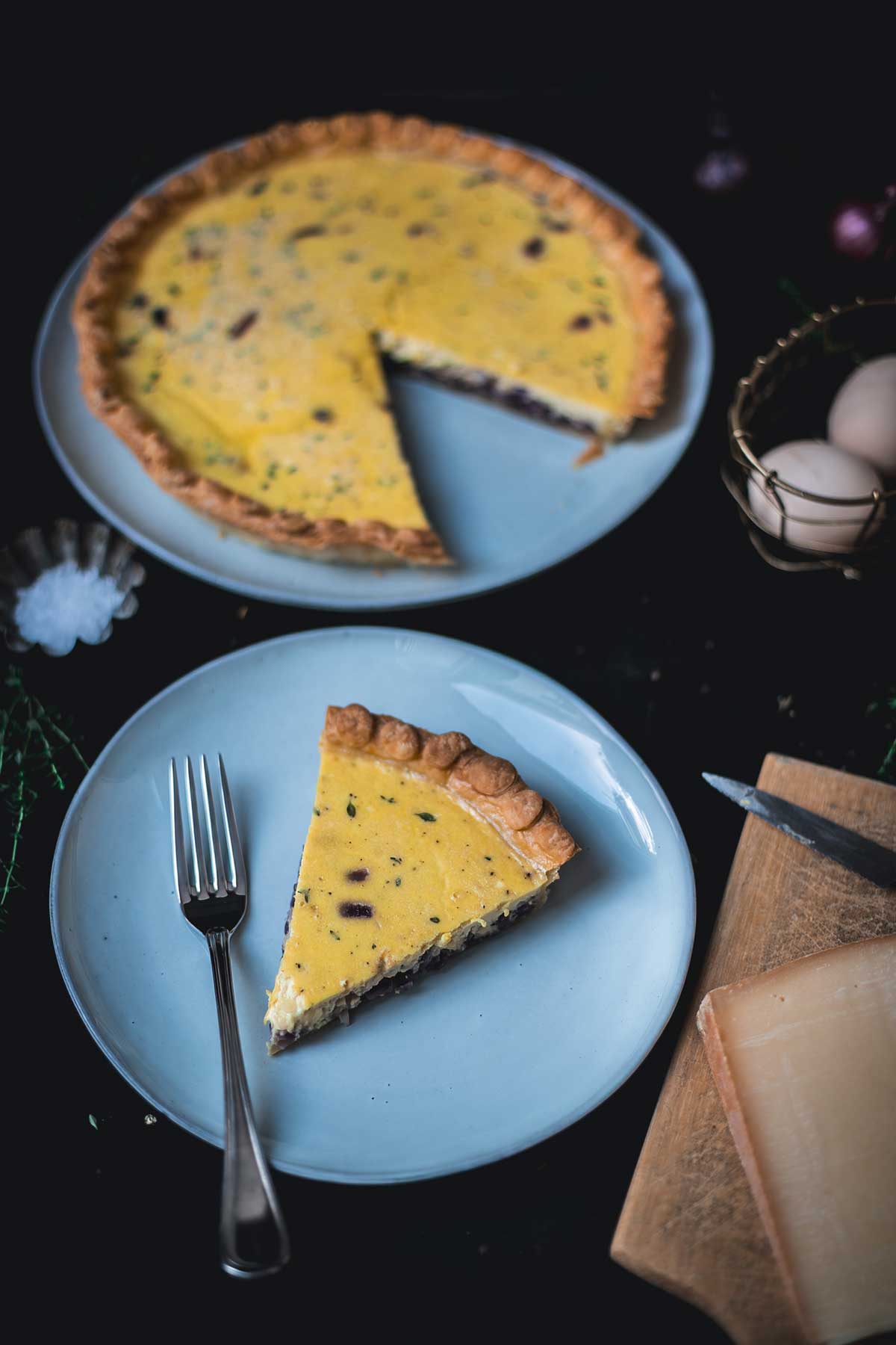 Stück Zwiebelquiche auf Teller im Fokus, im Hintergrund die Quiche mit Anschnitt, aus leicht anderem Winkel aufgenommen | moeyskitchen.com