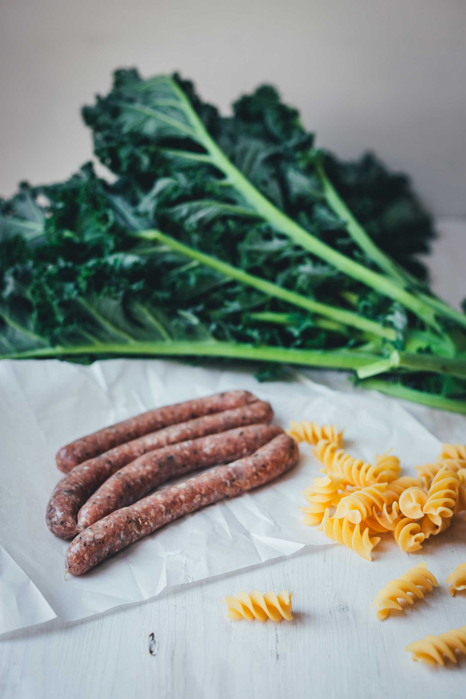 Ein Bund Grünkohl, ein paar frische grobe Bratwürste und trockene Pasta als Zutaten für das Pasta mit Grünkohl Gericht.