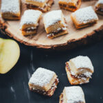 Bratapfel-Stollen-Konfekt in kleinen würfelförmigen Stücken, bestäubt mit Puderzucker, auf Holzbrett angerichtet.
