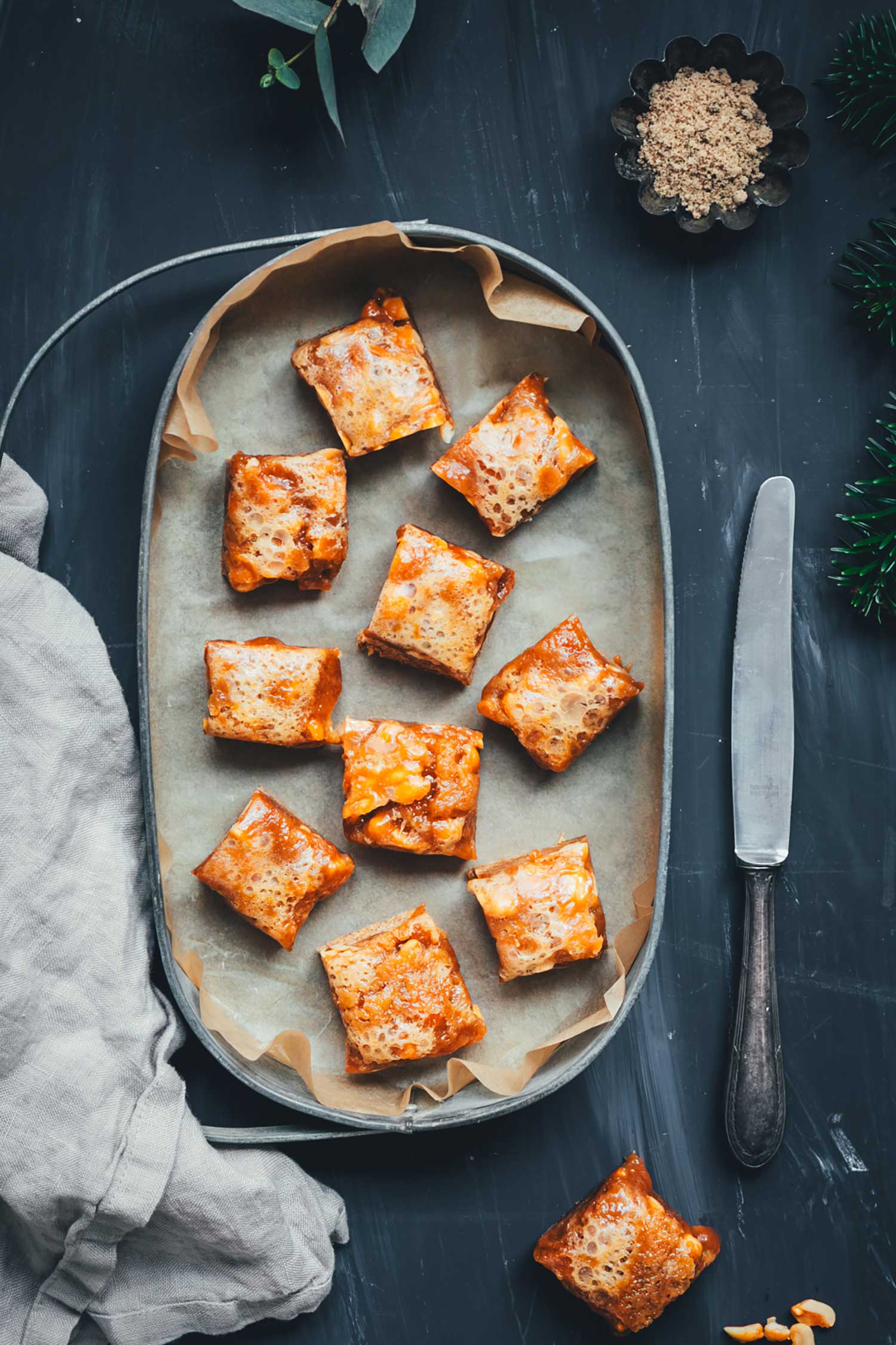 Lebkuchen-Karamell-Würfel auf einem Blech mit Backpapier, von oben fotografiert – weiche Karamellschicht und sichtbare Erdnüsse.