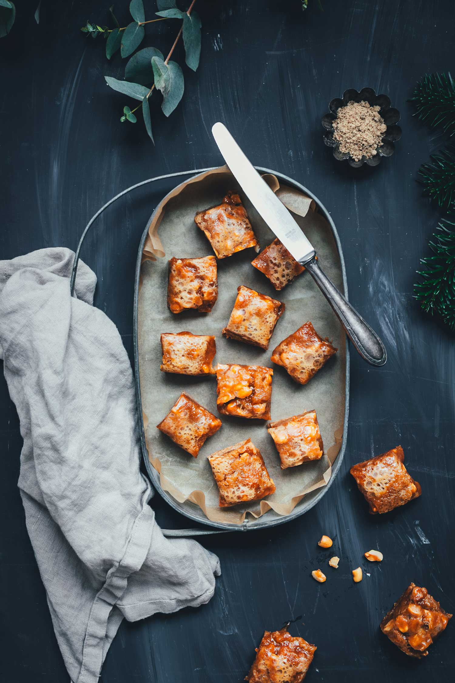 Tablett mit mehreren Lebkuchen-Karamell-Würfeln und Messer, stimmungsvolles Foodfoto in dunkler Umgebung.