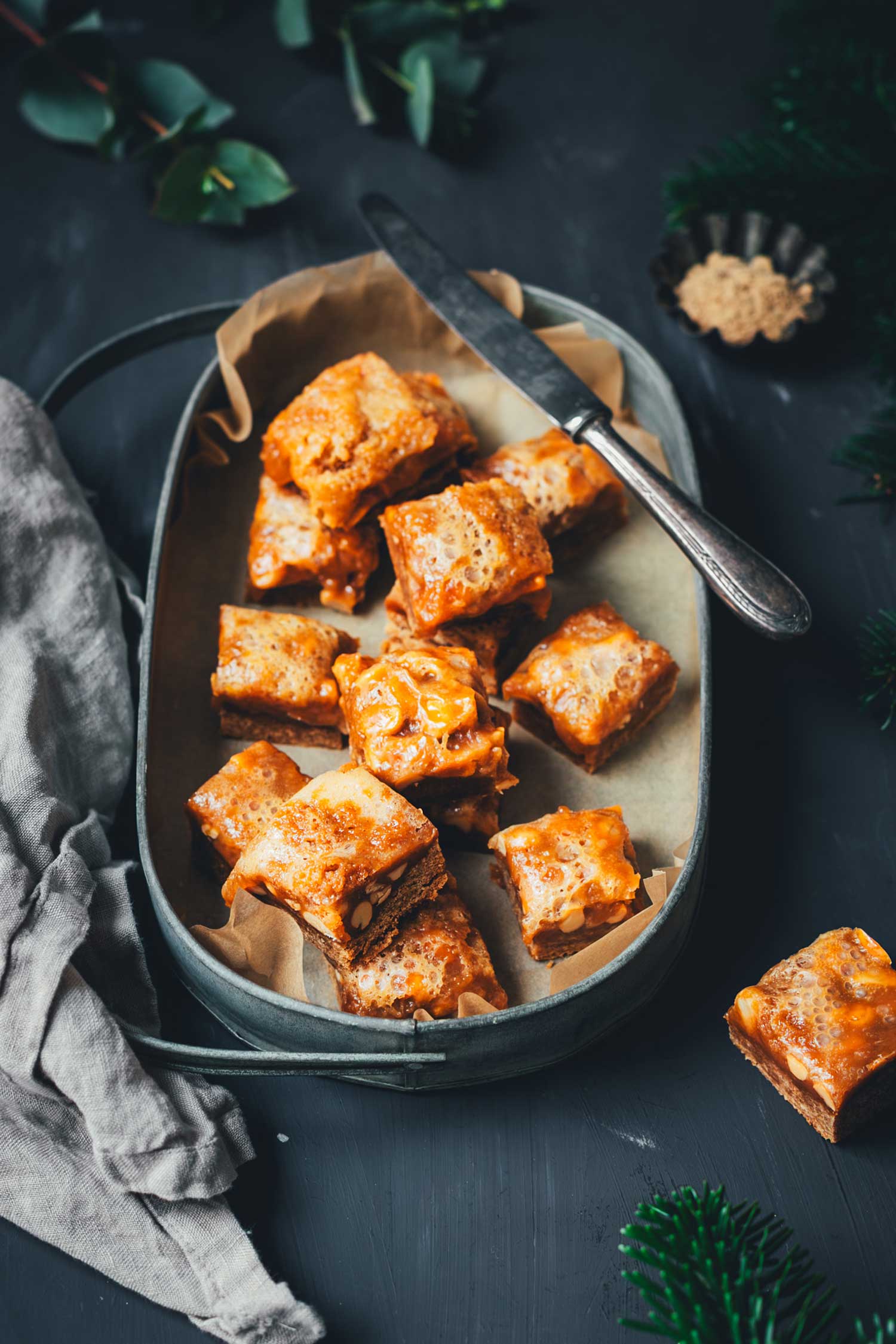 Lebkuchen-Karamell-Würfel in einer dunklen Metallschale, Nahaufnahme der Karamell- und Nussschicht.