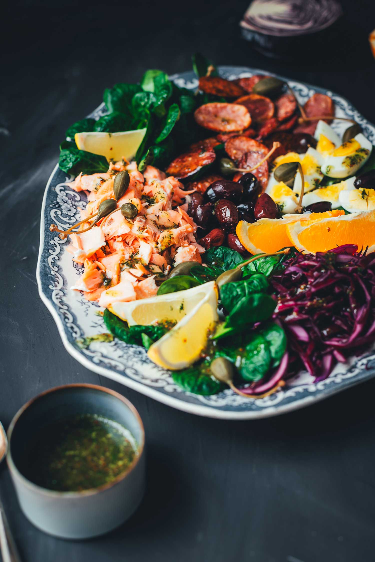 Halbschräge Ansicht Winterlicher Nizza Salat mit Pulled Lachs auf Servierplatte – mit Rotkohl, Feldsalat, knusprigen Kartoffeln, Eiern, Orangen und Kapernäpfeln.