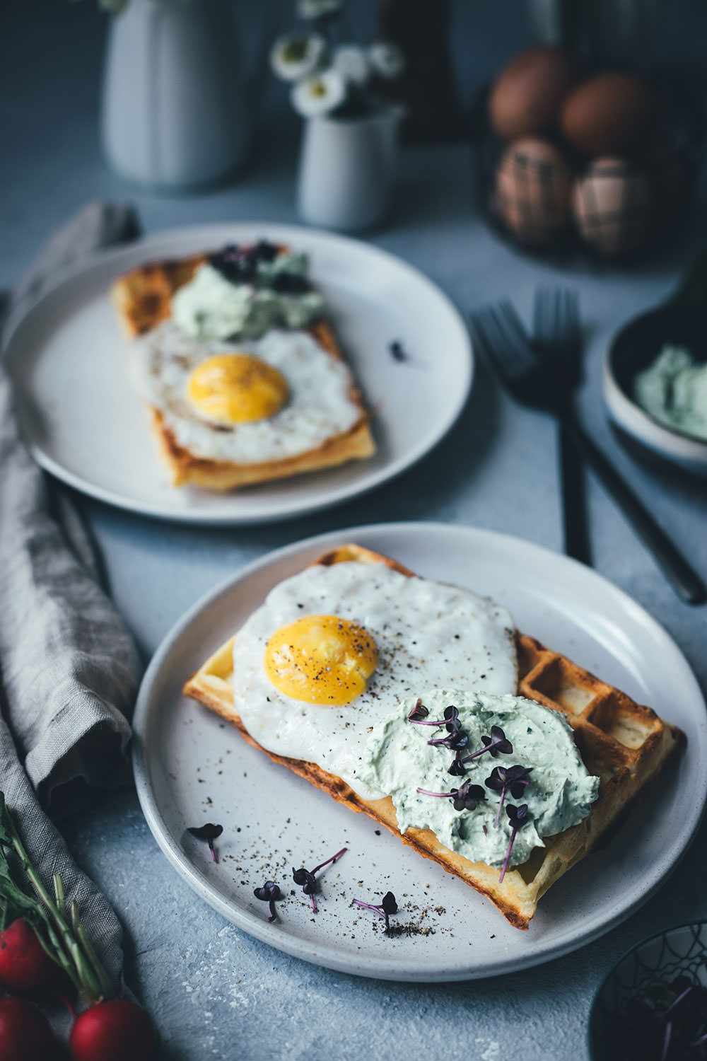 Ansicht von zwei Tellern, servierbereit mit frisch gebackenen Kartoffelwaffeln, getoppt mit Spiegelei und frischem Bärlauch-Dip.