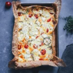 Zucchini-Frittata mit Feta und Tomaten aus dem Ofen, frisch gebacken in einer mit Backpapier ausgelegten Form, daneben Cherrytomaten und frischer Thymian.