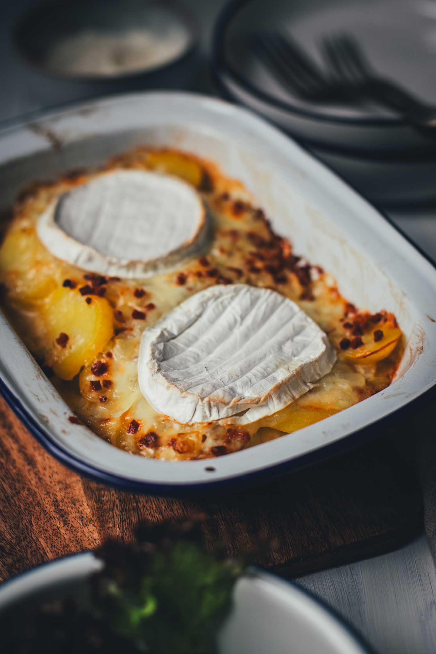 Nahaufnahme einer frisch gebackenen Tartiflette: Der Camembert ist perfekt geschmolzen und verbindet sich mit den goldbraunen Kartoffelscheiben und krossem Speck.