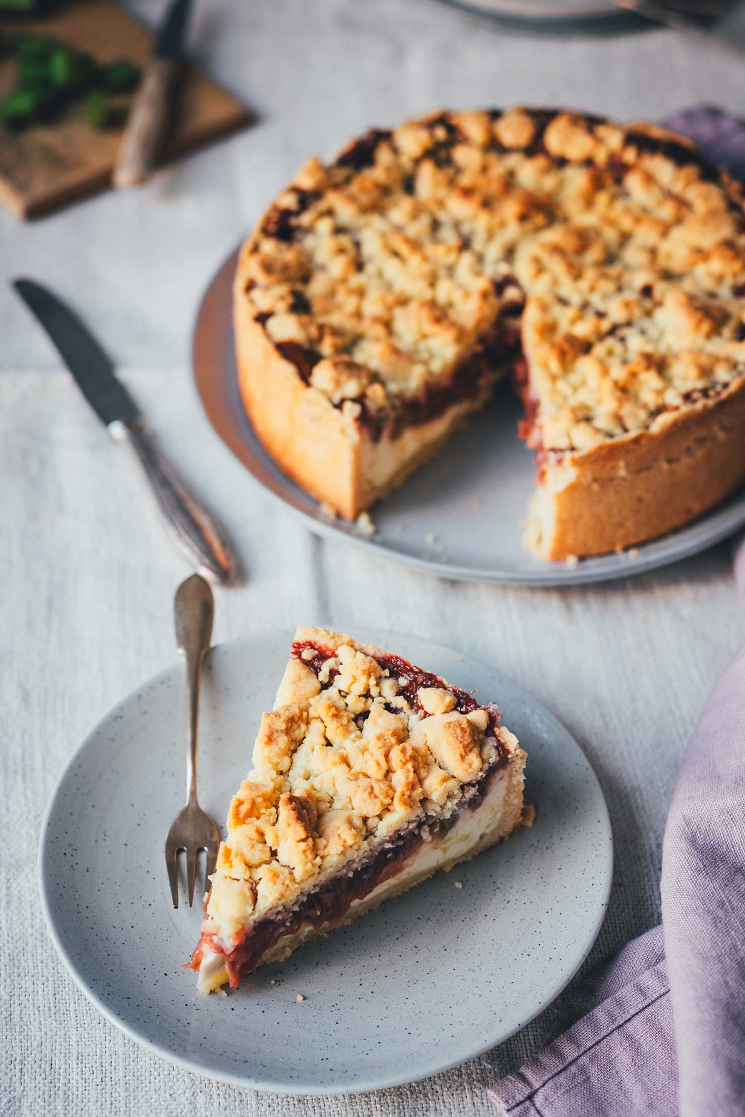 Stück Rhabarber-Käsekuchen mit Quarkfüllung und Streuseln auf einem Dessertteller mit Gabel