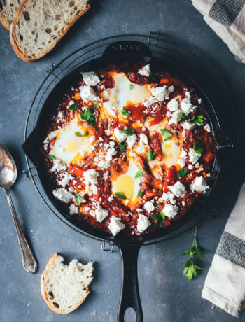 Topshot einer Pfanne mit Shakshuka aus dem Ofen. Eier in Tomaten-Paprika-Sauce geschmort und mit Feta und Petersilie bestreut serviert | moeyskitchen.com