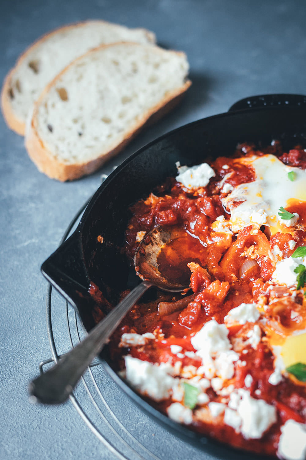 seitlich fotografierter Pfannenanschnitt von fertig gegarter Shakshuka aus dem Ofen mit Eiern und Feta und knusprigem Brot | moeyskitchen.com