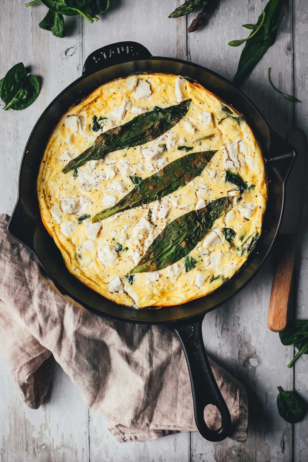 Topshot-Aufnahme von Bärlauch-Frittata mit grünem Spargel, Spinat und Feta direkt in der gusseisernen Pfanne serviert.