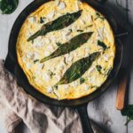 Topshot-Aufnahme von Bärlauch-Frittata mit grünem Spargel, Spinat und Feta direkt in der gusseisernen Pfanne serviert.