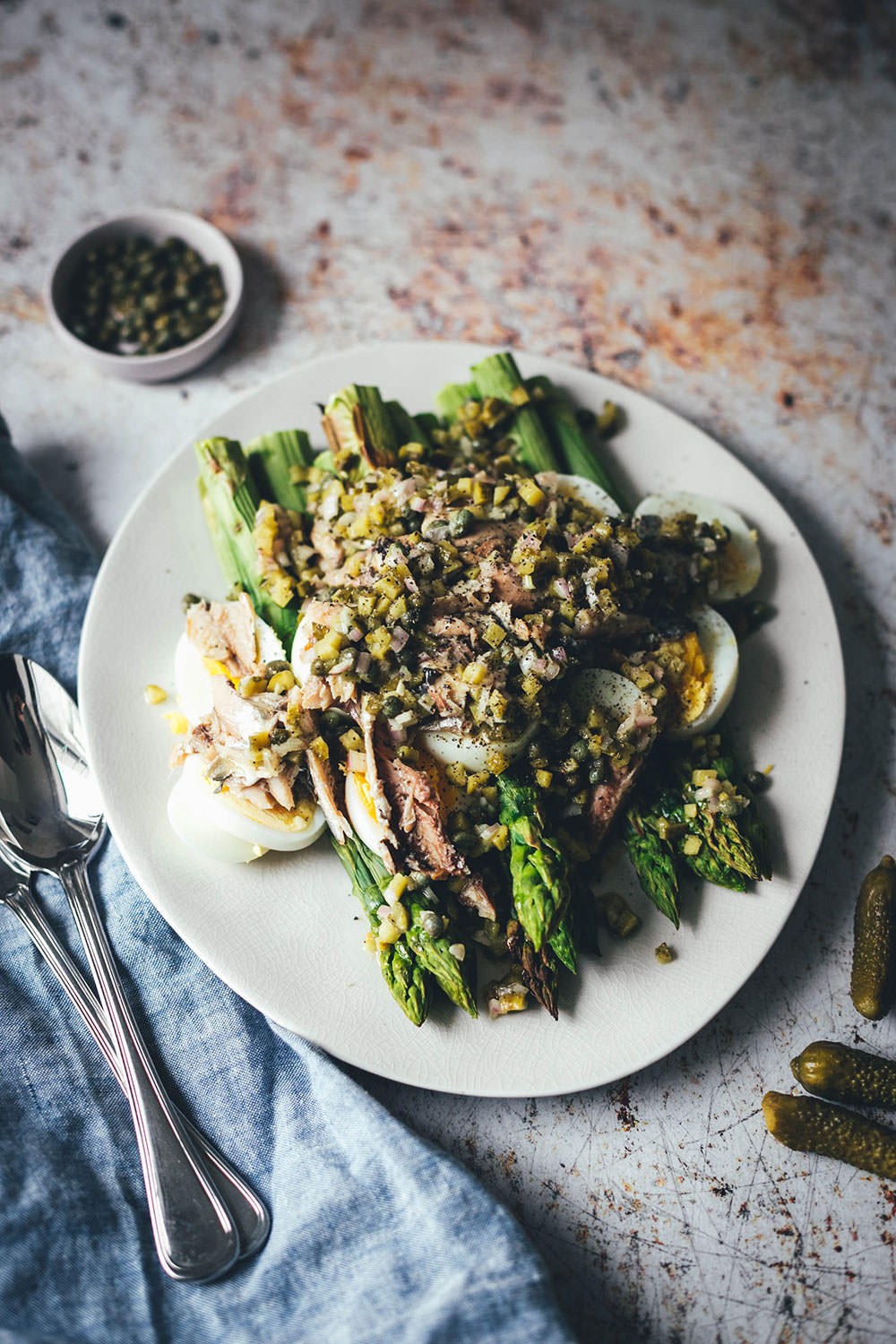 Rezept für würzigen Spargelsalat aus ofengeröstetem grünen Spargel mit einer Kapern-Vinaigrette, Sardinen und Ei. Blitzschnell auf dem Tisch und mit knusprigem Brot und einem Glas kühlen Weißwein perfekt für laue Frühlings- oder Sommerabende auf dem Balkon! Würzige Kapern, Cornichons und Schalotten geben der Vinaigrette Pfiff und harmonieren fantastisch zu den Ölsardinen aus der Dose und dem hart gekochten Ei | moeyskitchen.com
