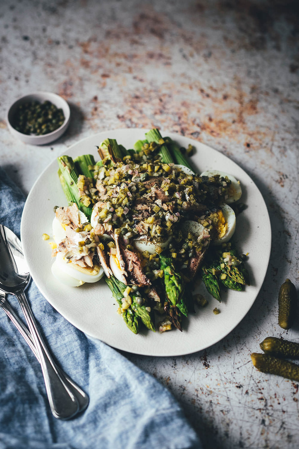Rezept für würzigen Spargelsalat aus ofengeröstetem grünen Spargel mit einer Kapern-Vinaigrette, Sardinen und Ei. Blitzschnell auf dem Tisch und mit knusprigem Brot und einem Glas kühlen Weißwein perfekt für laue Frühlings- oder Sommerabende auf dem Balkon! Würzige Kapern, Cornichons und Schalotten geben der Vinaigrette Pfiff und harmonieren fantastisch zu den Ölsardinen aus der Dose und dem hart gekochten Ei | moeyskitchen.com