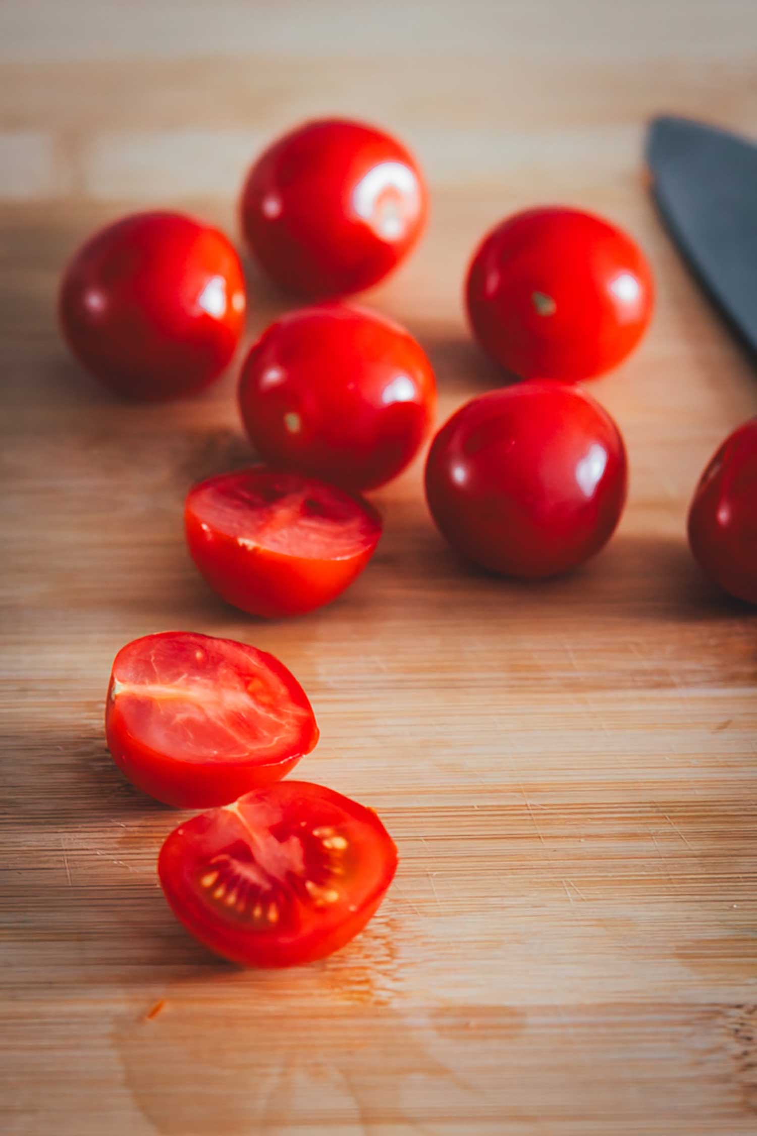 Cocktailtomaten werden auf einem Schneidebrett halbiert.