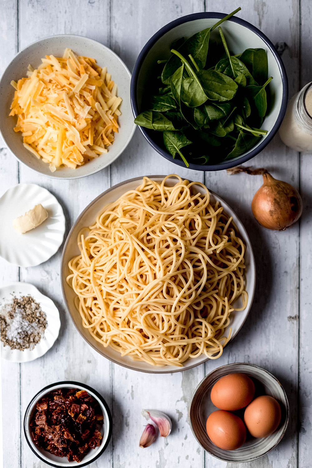 Top-Shot-Aufnahme aller Zutaten für den Spaghetti-Kuchen: gekochte Nudeln, Spinat, Eier, Cheddar usw.