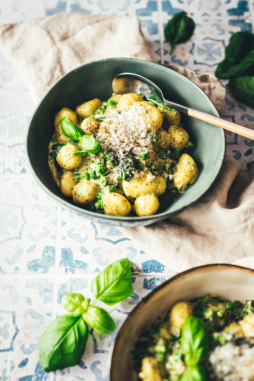 Nahaufnahme eines Tellers mit cremiger Gnocchi-Pfanne mit Erbsen, Spinat und reichlich Käse. Abgeschmeckt mit Pesto und Basilikum und servierbereit