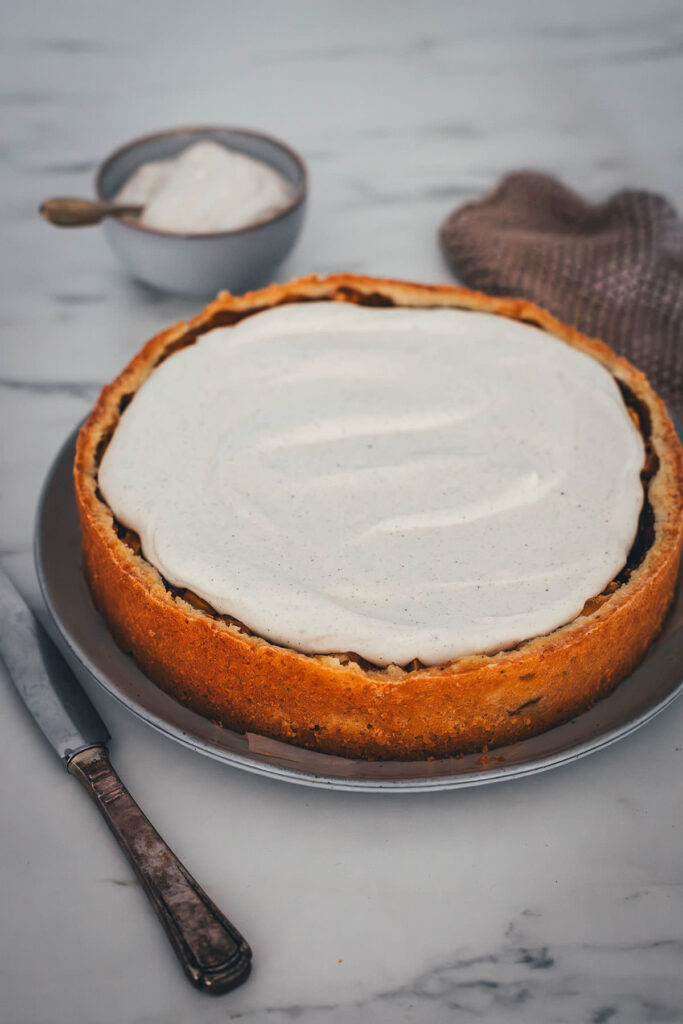 Rezept für Apfelkuchen mit knusprigem Mürbeteigboden und einer Füllung mit Äpfeln. Vanillepuddingpulver wird hier einfach mit Apfelsaft angerührt und mit Apfelstückchen gefüllt. Das ergibt die köstliche Füllung für diesen simplen Apfel-Pudding-Kuchen. Getoppt wird der Kuchen dann mit einer ganz lockeren Schmandcreme mit Vanille. | moeyskitchen.com