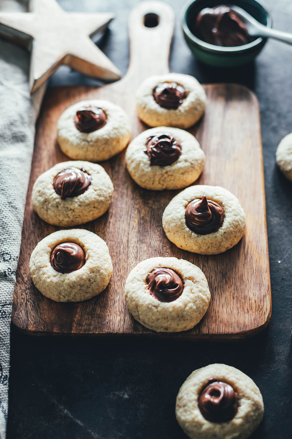 Entzückende Haselnussplätzchen, mit Nuss-Nougat-Creme gefüllt und auf einem Hokzbrett drapiert. Im Hintergrund Weihnachtsdeko.