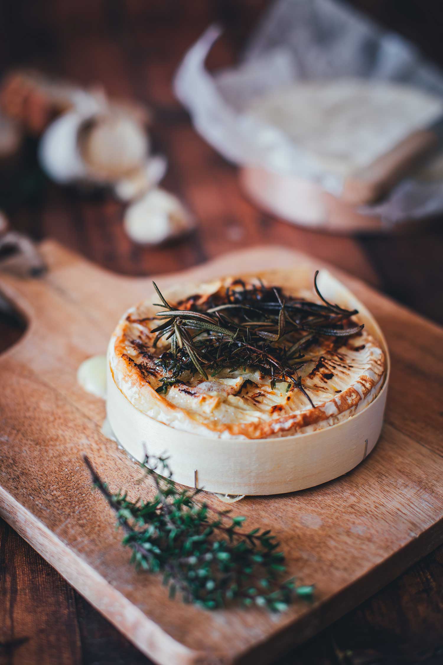 Servierfertiger gebackener Camembert mit Honig-Rosmarin-Topping auf einem rustikalen Holzbrett mit frischem Thymian.