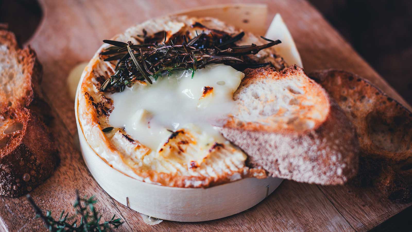 Gebackener Camembert aus der Heißluftfritteuse mit flüssigem Kern, getoppt mit geröstetem Rosmarin und serviert mit Baguette auf einem Holzbrett.