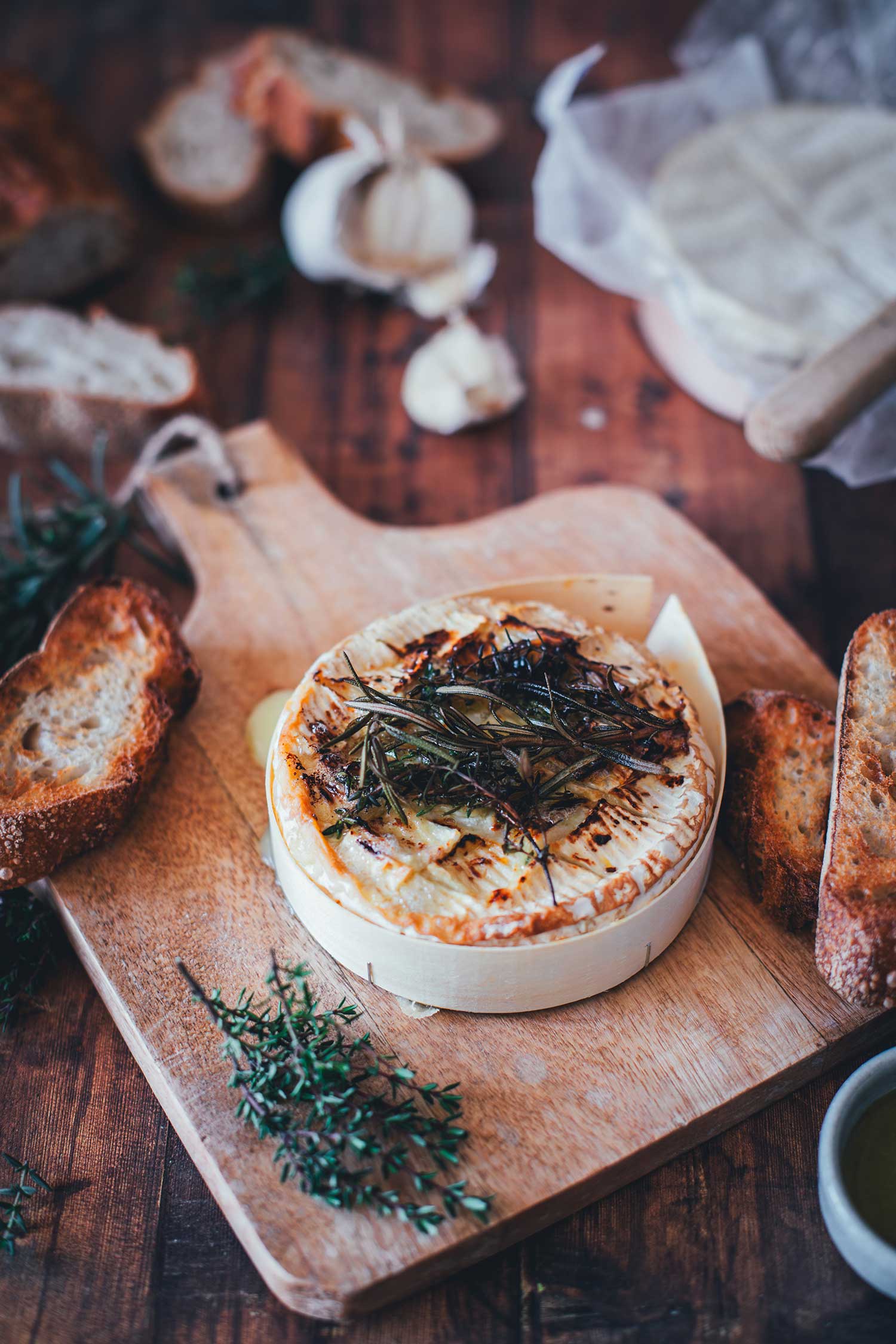 Als Ofenkäse im Airfryer gebackener Camembert mit Honig-Rosmarin-Topping auf einem rustikalen Holzbrett mit frischem Thymian.
