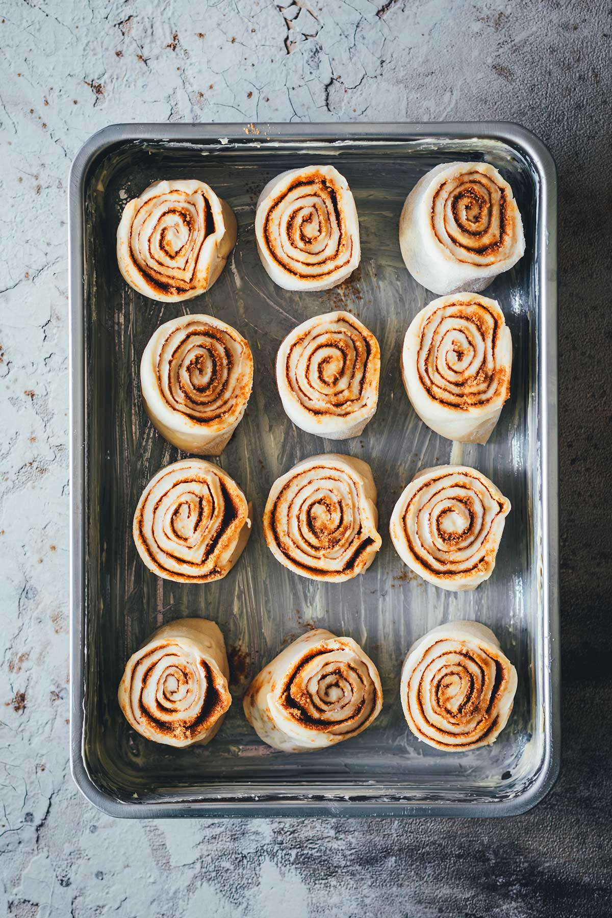 Rohe Cinnamon Rolls liegen in einer gefetteten Auflaufform bereit für die Übernacht-Gare im Kühlschrank.