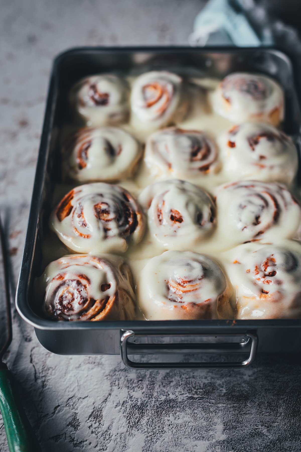 Eine Backform ist mit fertig gebackene Soft Cinnamon Rolls gefüllt und mit Frischkäse-Frosting bestrichen