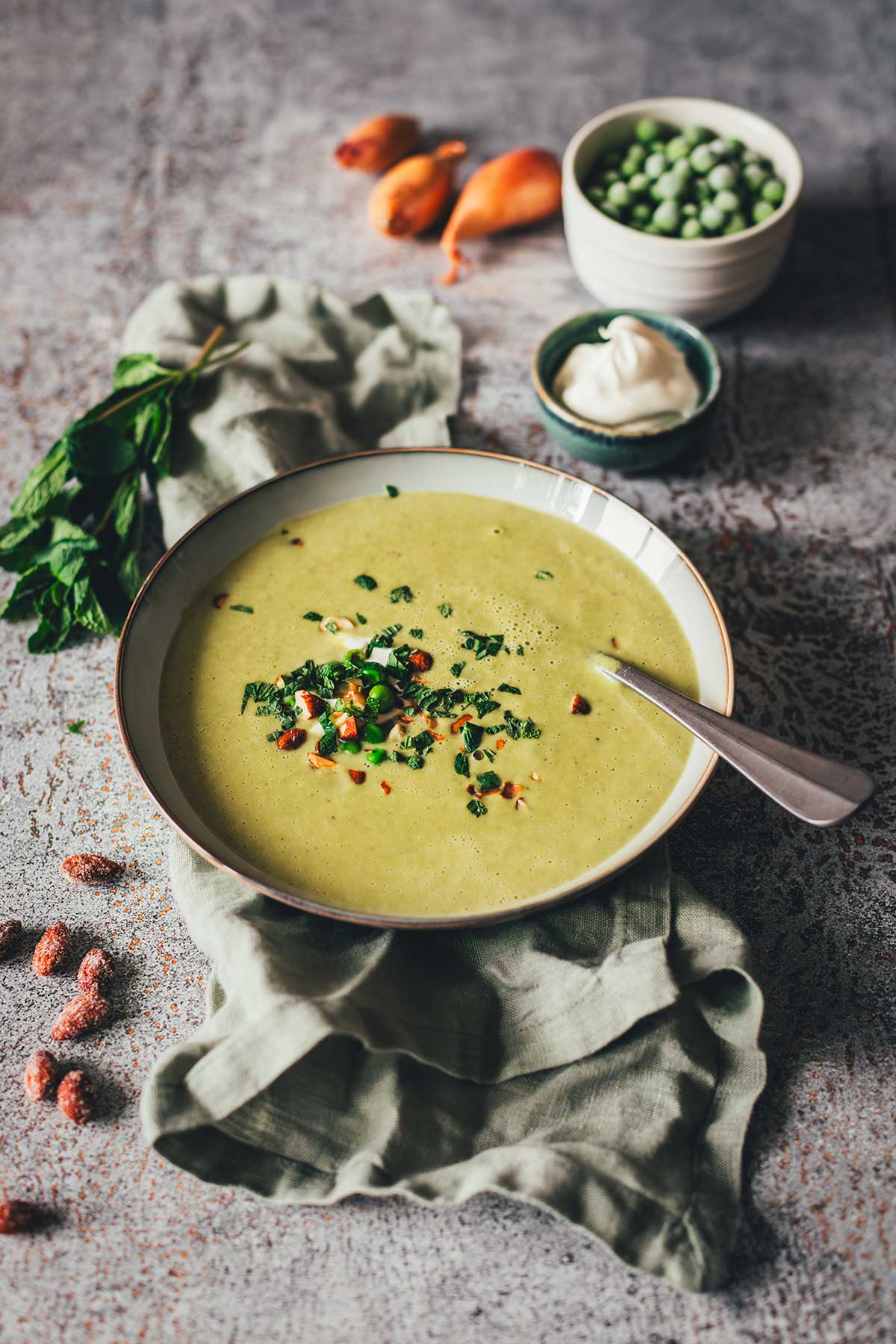Erbsensuppe mit Minze und Crème fraîche in einer Schale, garniert mit Kräutern und Mandeln. | moeyskitchen.com
