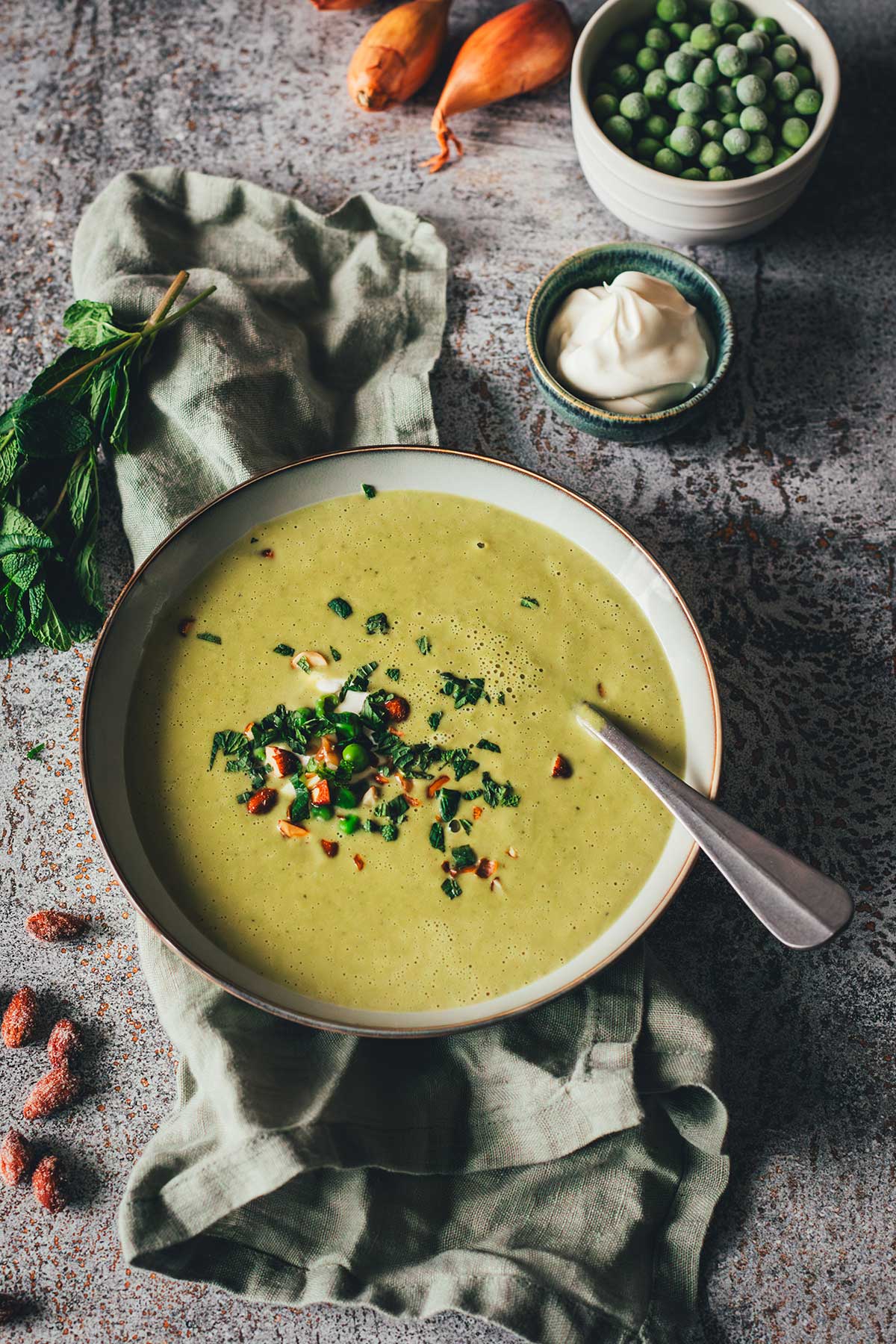 Erbsensuppe mit Minze und Crème fraîche in einer Schale, garniert mit Kräutern und Mandeln. | moeyskitchen.com