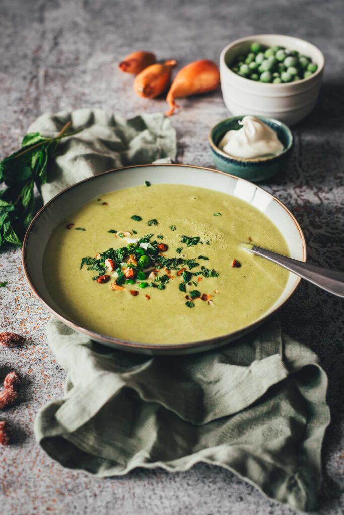 Erbsensuppe mit Minze und Crème fraîche in einer Schale, garniert mit Kräutern und Mandeln. | moeyskitchen.com