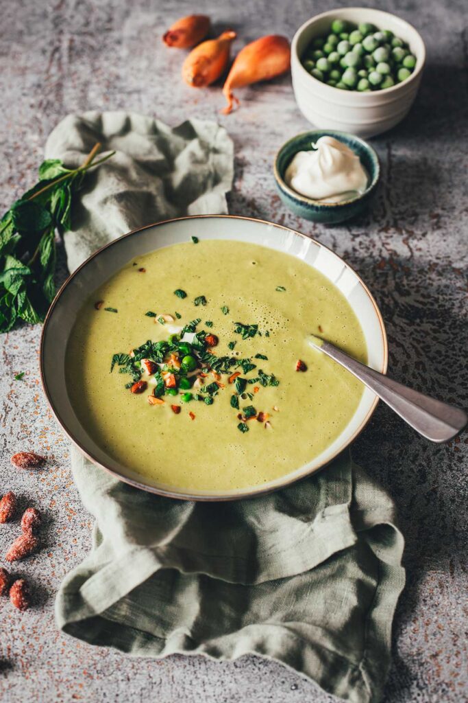 Erbsensuppe mit Minze und Crème fraîche in einer Schale, garniert mit Kräutern und Mandeln. | moeyskitchen.com