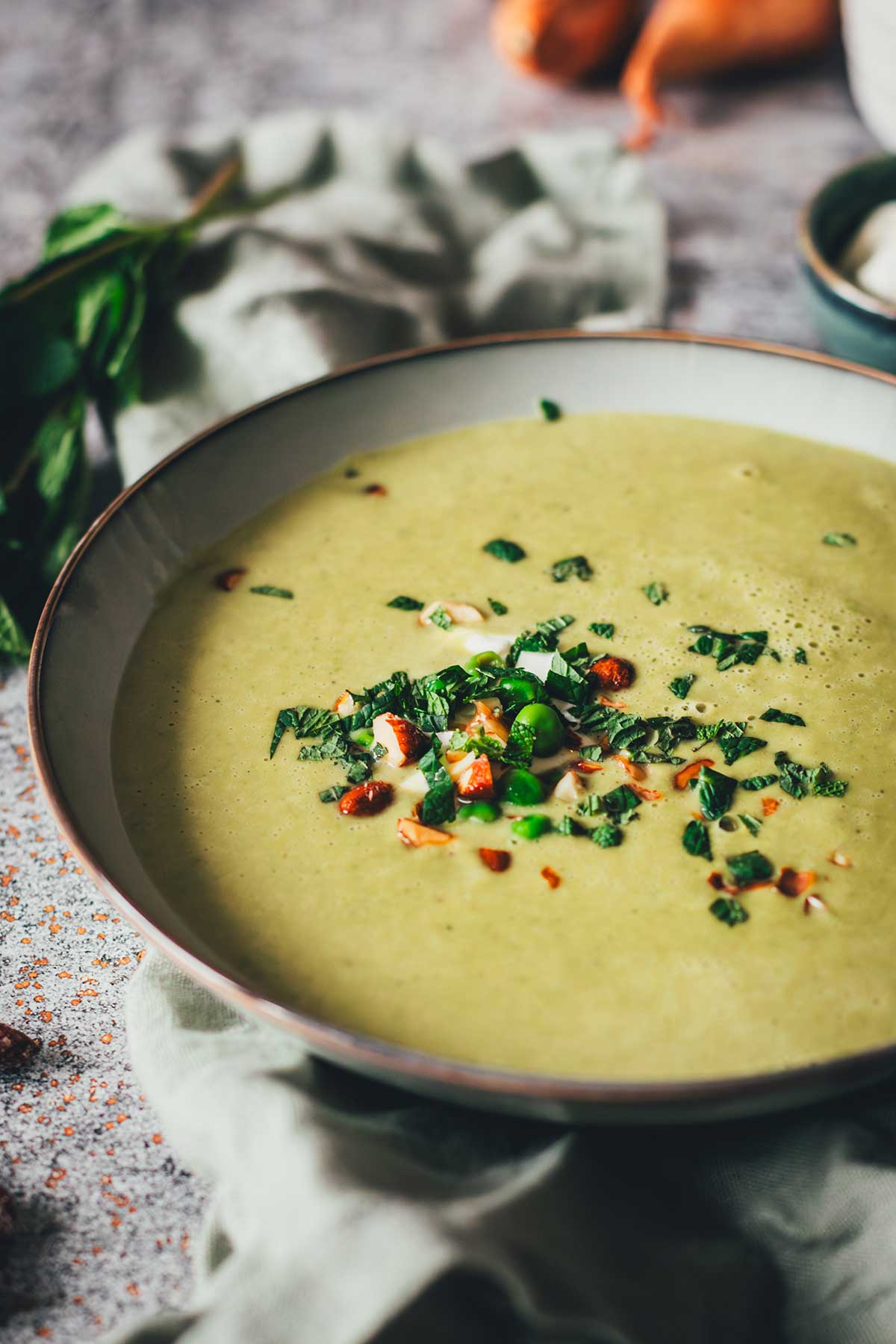 Erbsensuppe mit Minze und Crème fraîche in einer Schale, garniert mit Kräutern und Mandeln. | moeyskitchen.com