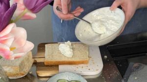 Ansichter einer waagerechten Scheibe vom Kastenweißbrot, das jetzt mit der angerührten Frischkäsecreme bestrichen wird.